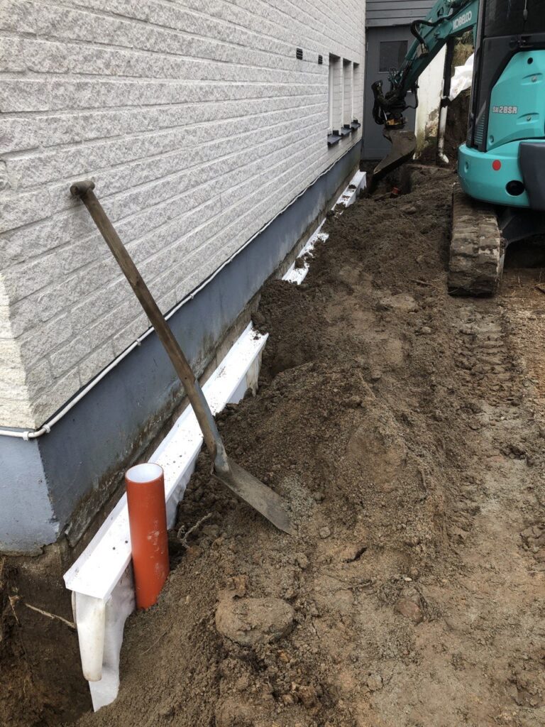 Återfyllning längs husgrund efter installation av dräneringssystem i Trollhättan.
