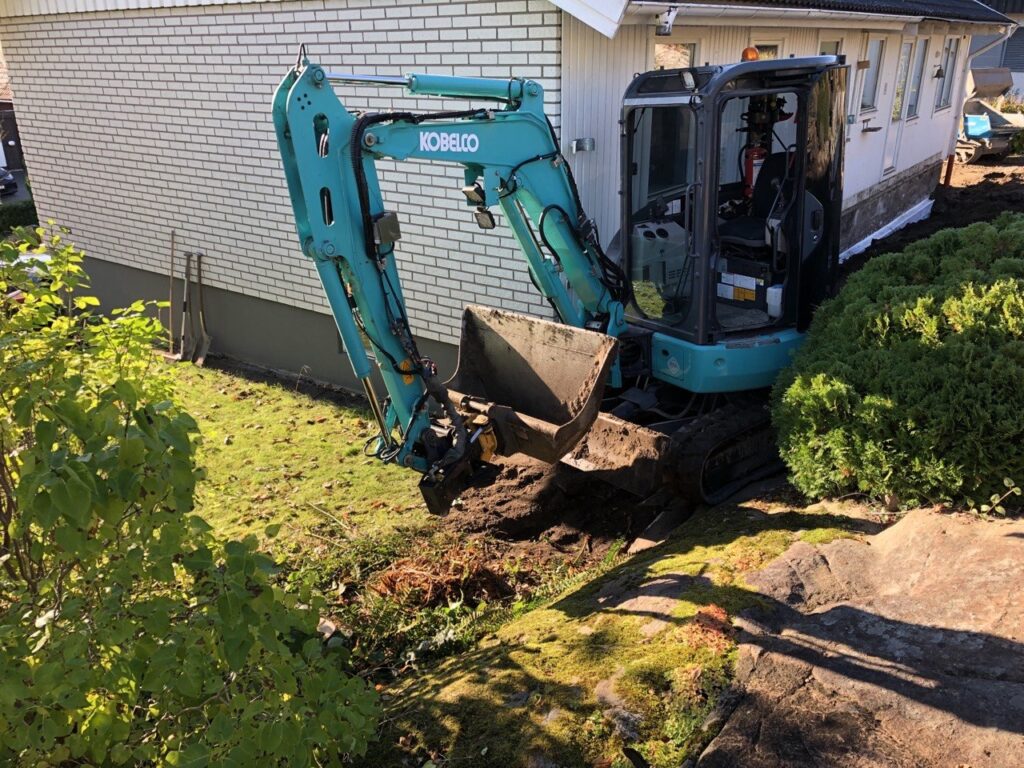 Minigrävare arbetar intill husgrund under dräneringsarbete i Trollhättan.