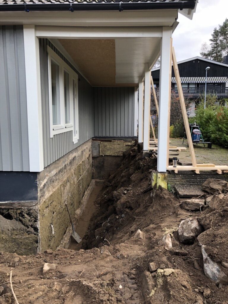 Dräneringsschakt längs husgrund under täckt uteplats.