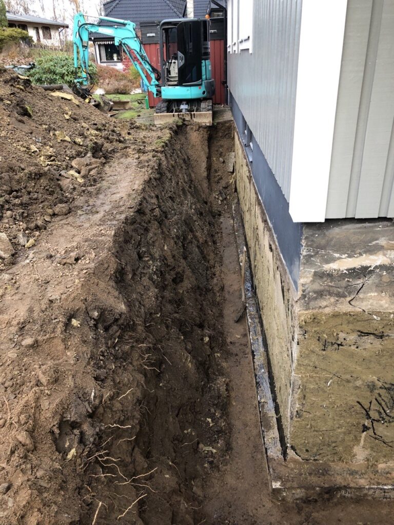 Schakt längs husgrund inför installation av nytt dräneringssystem.